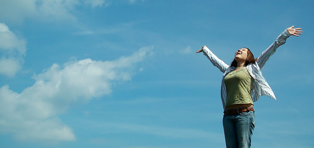 Foto di Jess Hall. Una ragazza con le braccia aperte davanti a un cielo azzurro. Foto di Jess Hall.